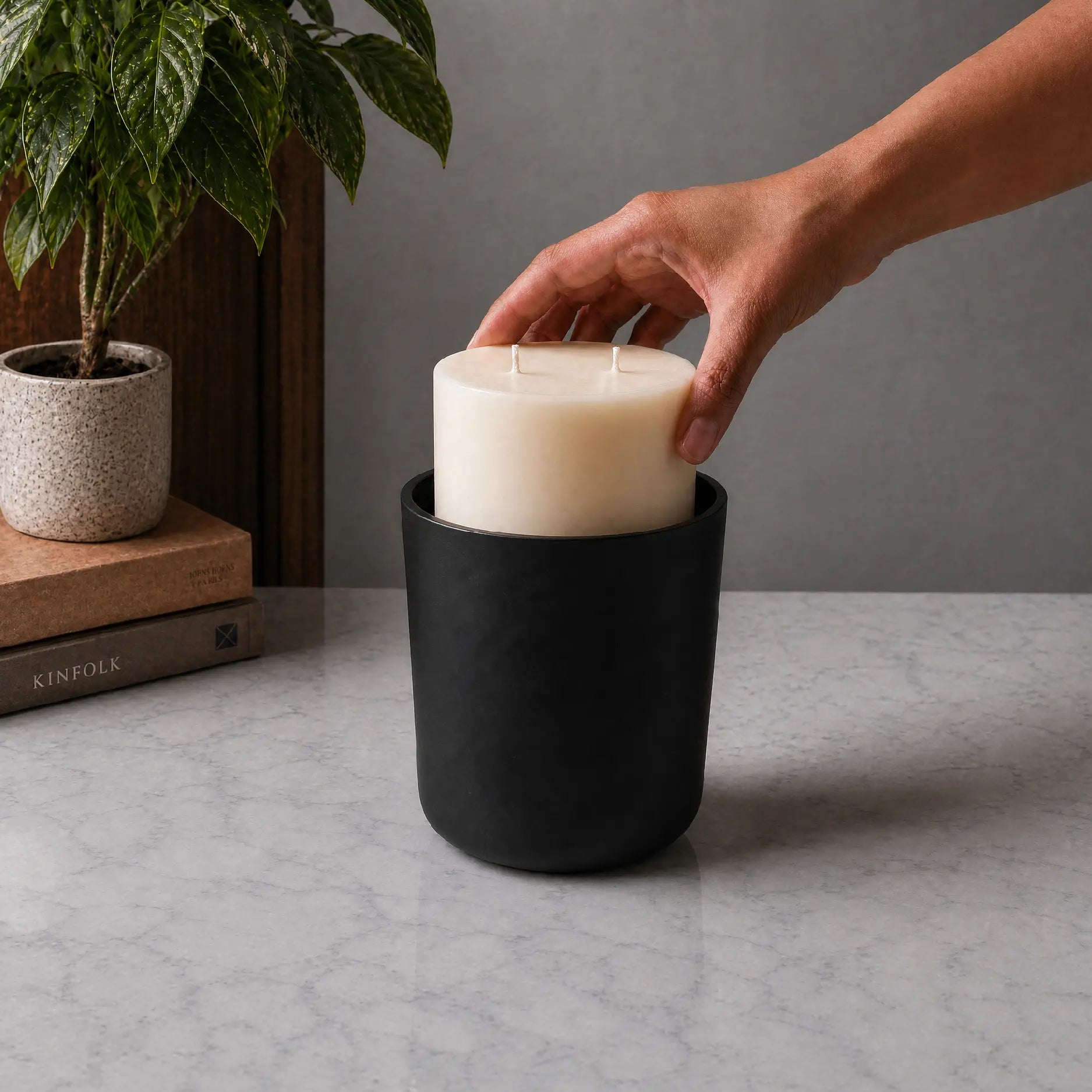 Hand inserting Wild Journey studio candle drop-in refill into a black candle vessel